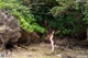 A woman in a red bikini standing on a rocky beach.